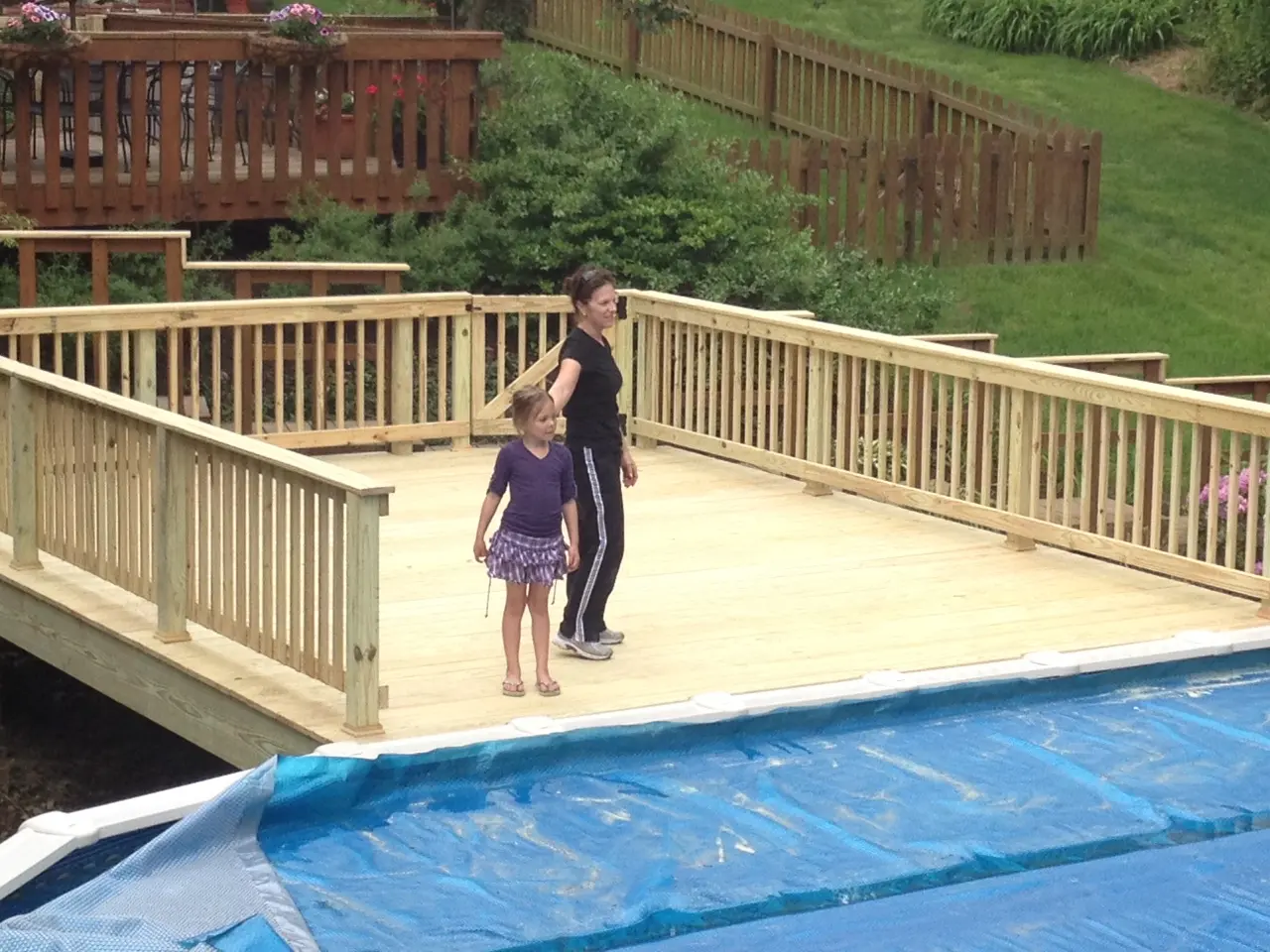 A woman and child standing on the deck of a pool.