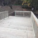 A wooden deck with railing and steps in the middle of it.