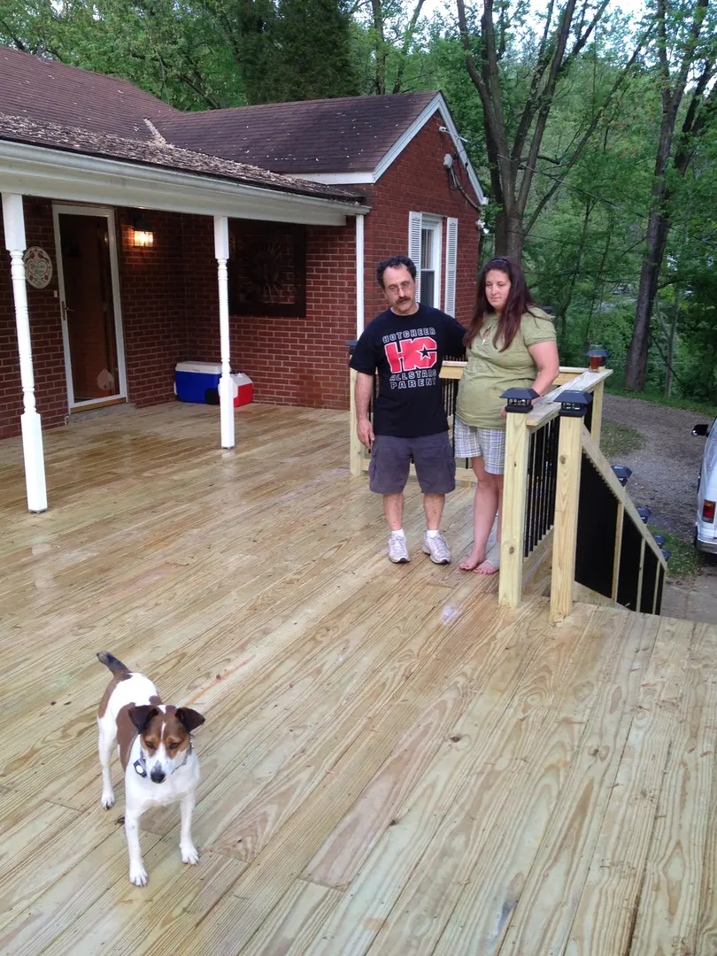 A man and woman standing on the porch of their home with a dog.