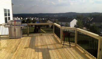 A wooden deck with black metal railing and a view of the city.