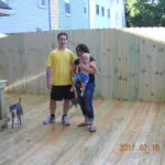 A man, woman and baby standing in front of a fence.