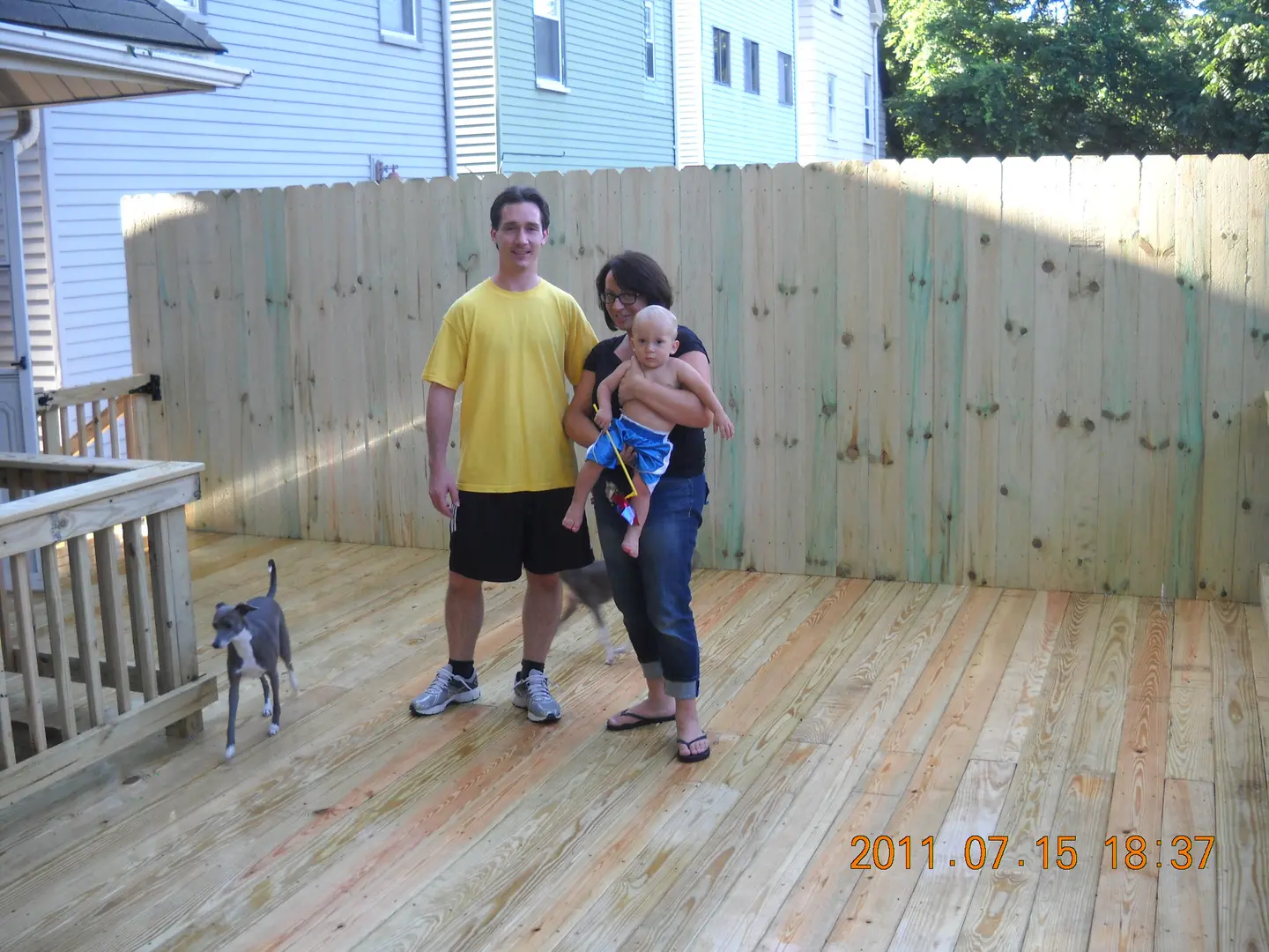 A man, woman and baby standing in front of a fence.