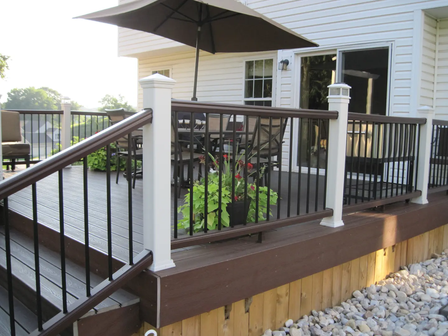 A deck with an umbrella and plants on the side.